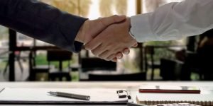Two people shaking hands over a desk with papers on it.