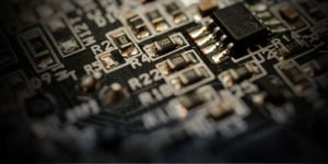 Close-up view of a dark microchip circuit board, showing detailed electronic components like resistors and integrated circuits, highlighting the complexity of semiconductor technology.
