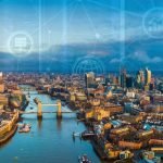 Aerial view of central London with Tower Bridge and the City skyline, overlaid with digital network icons symbolising connected infrastructure and technology.
